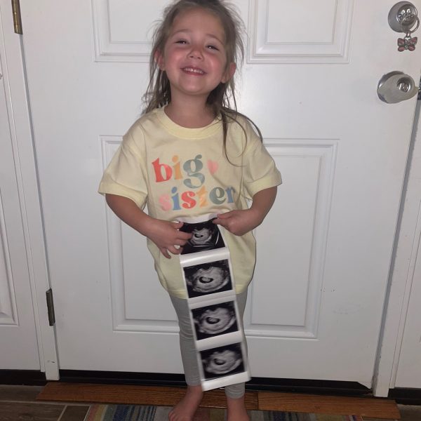 Girl holding ultrasound photos, smiling.